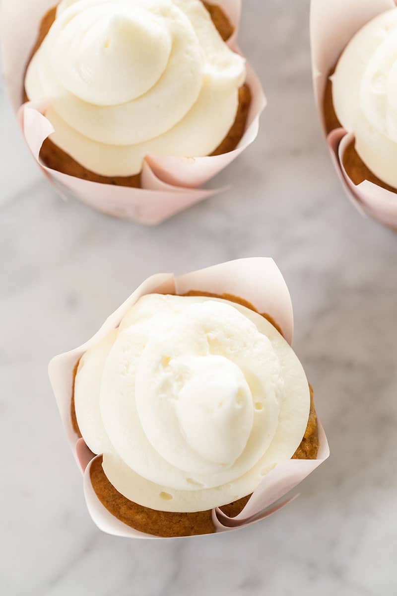 Carrot cake cupcakes with cream cheese frosting on a marble table.