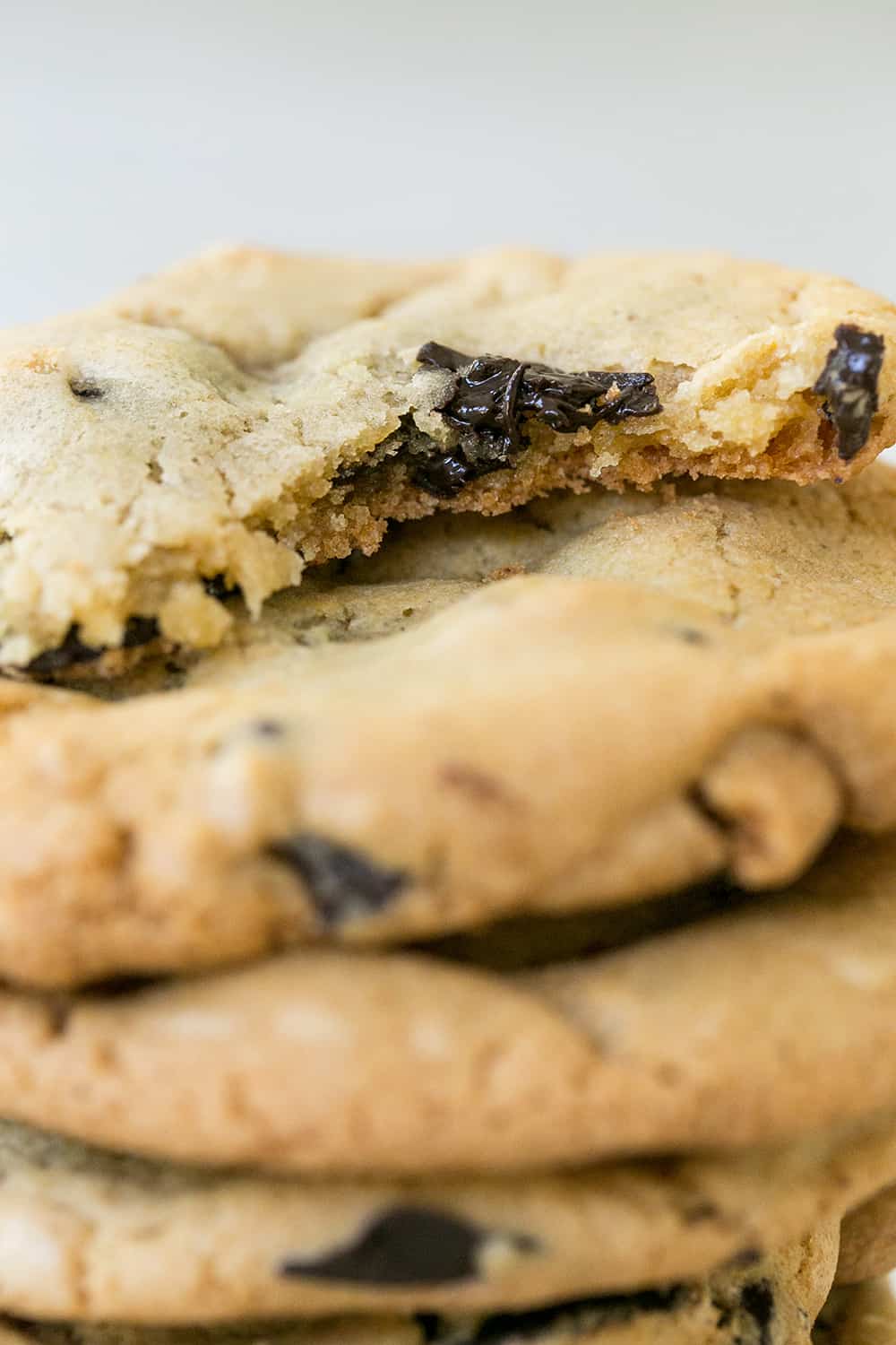 Chocolate chip cookies made with oil, and a bite is taken out, and a gooey chocolate chip is melted. 