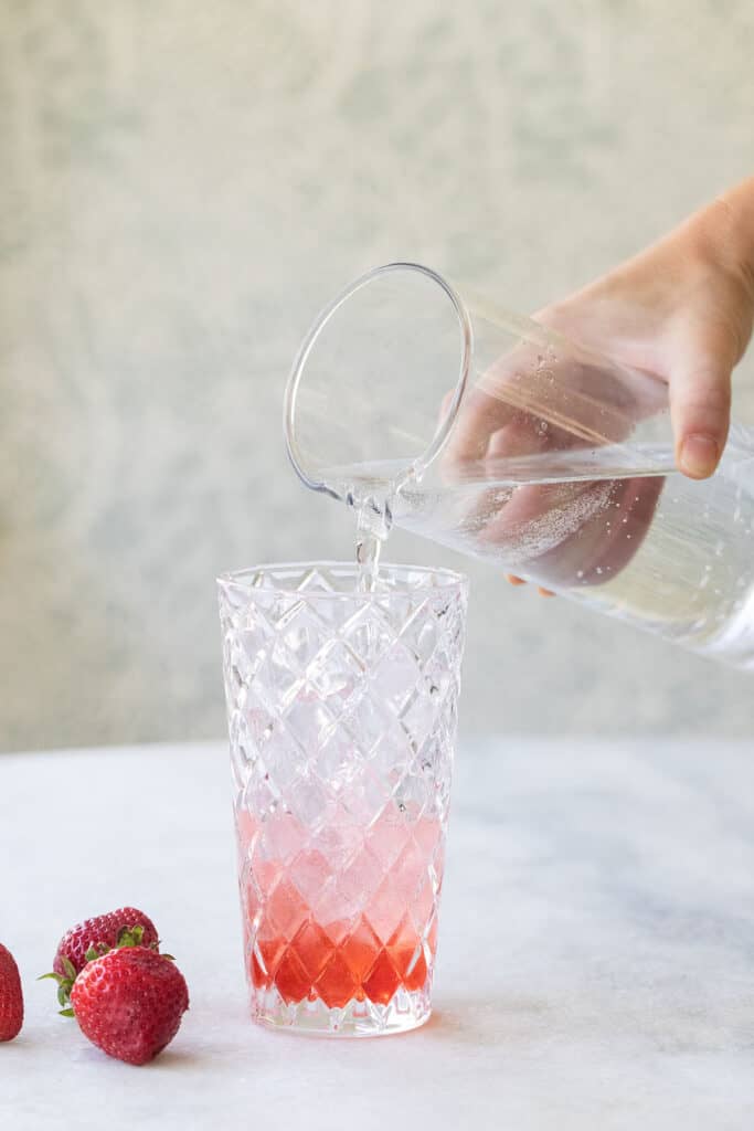 pouring soda water over ice and strawberry syrup in a glass