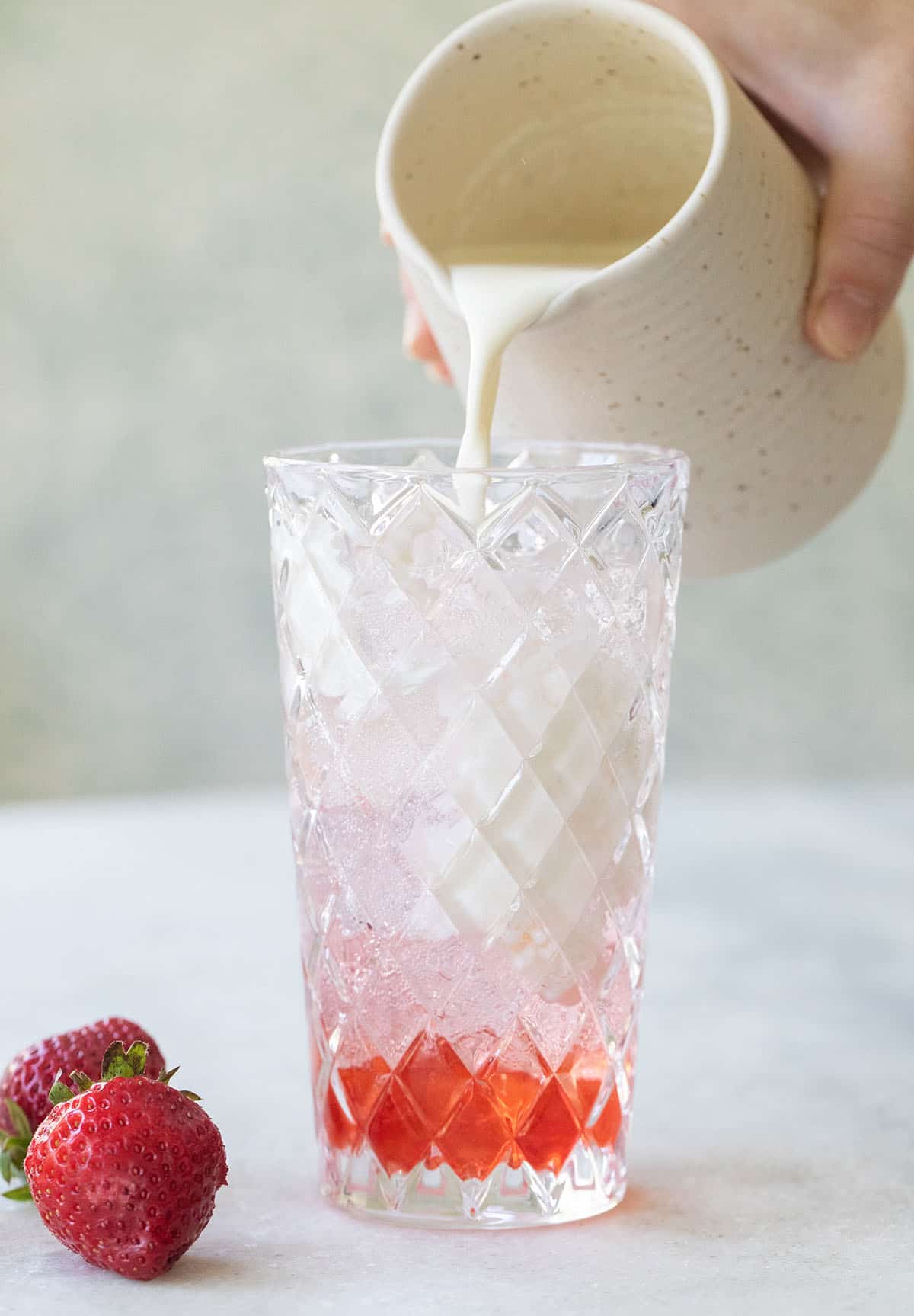 Pouring cream into a glass filled with ice and strawberry syrup to make an Italian soda.