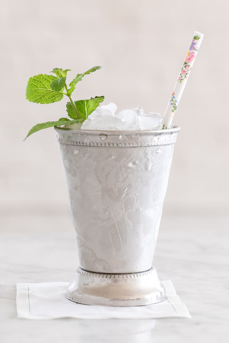 Cocktail in a silver cup with a straw, mint and ice