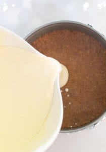 Pouring goat cheese batter into a graham cracker crust to make a creamy cheesecake recipe.