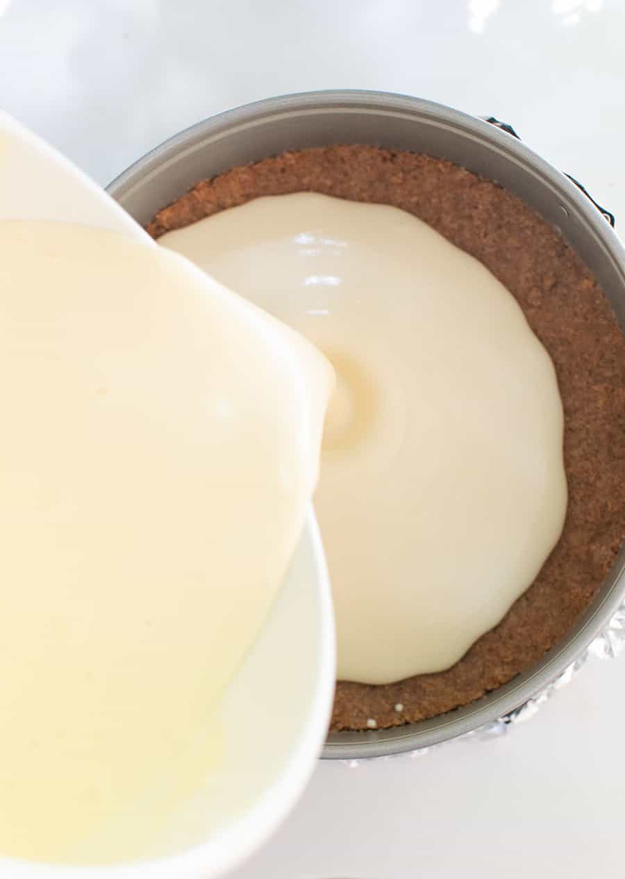 Pouring cheesecake batter over graham cracker crust.