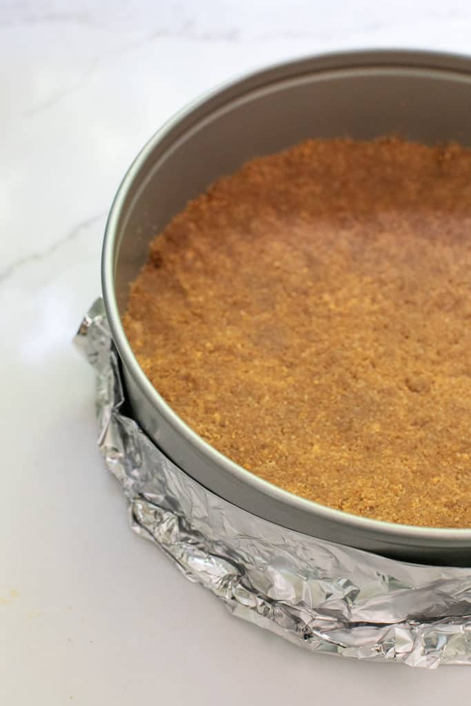 A buttery Graham Cracker crust pressed into a springform pan with tin foil around the sides for a water bath.