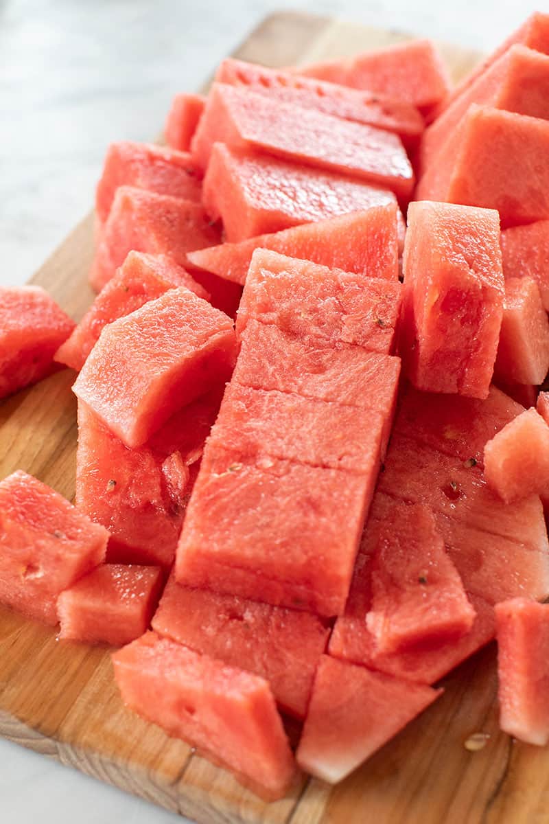 Watermelon cut into cubes on a cutting board.