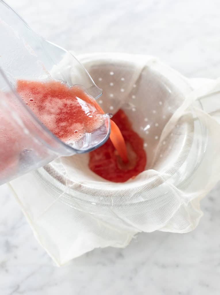 Pouring fresh watermelon juice into a strainer. 