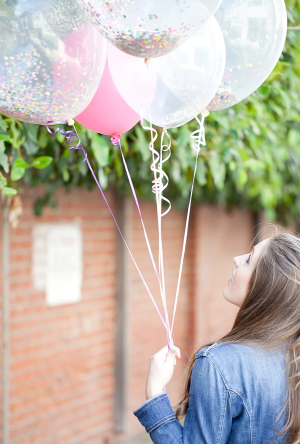 Girl holding 5 balloons filled with money and confetti.