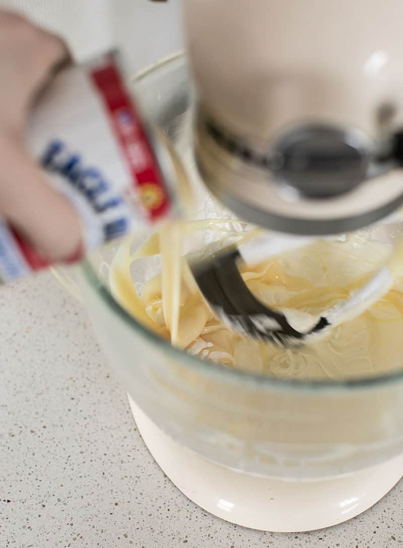 sweetened condensed milk being poured into an electric mixer.