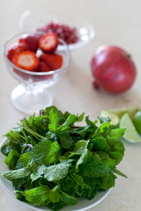 Fresh mint in a bowl with strawberries and a pomegranate in the back to make strawberry mojitos. 