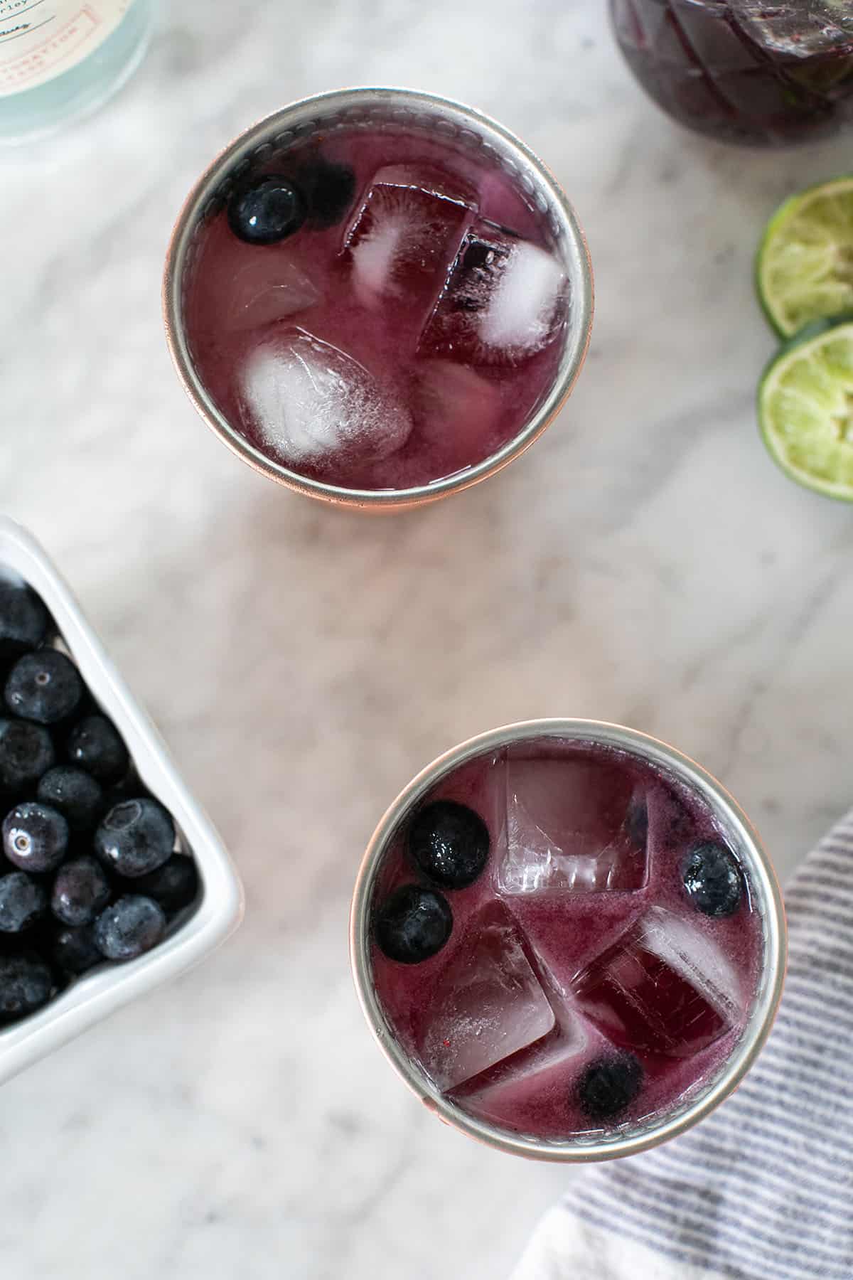 Two blueberry Moscow mules in copper mugs with ice and fresh blueberries.