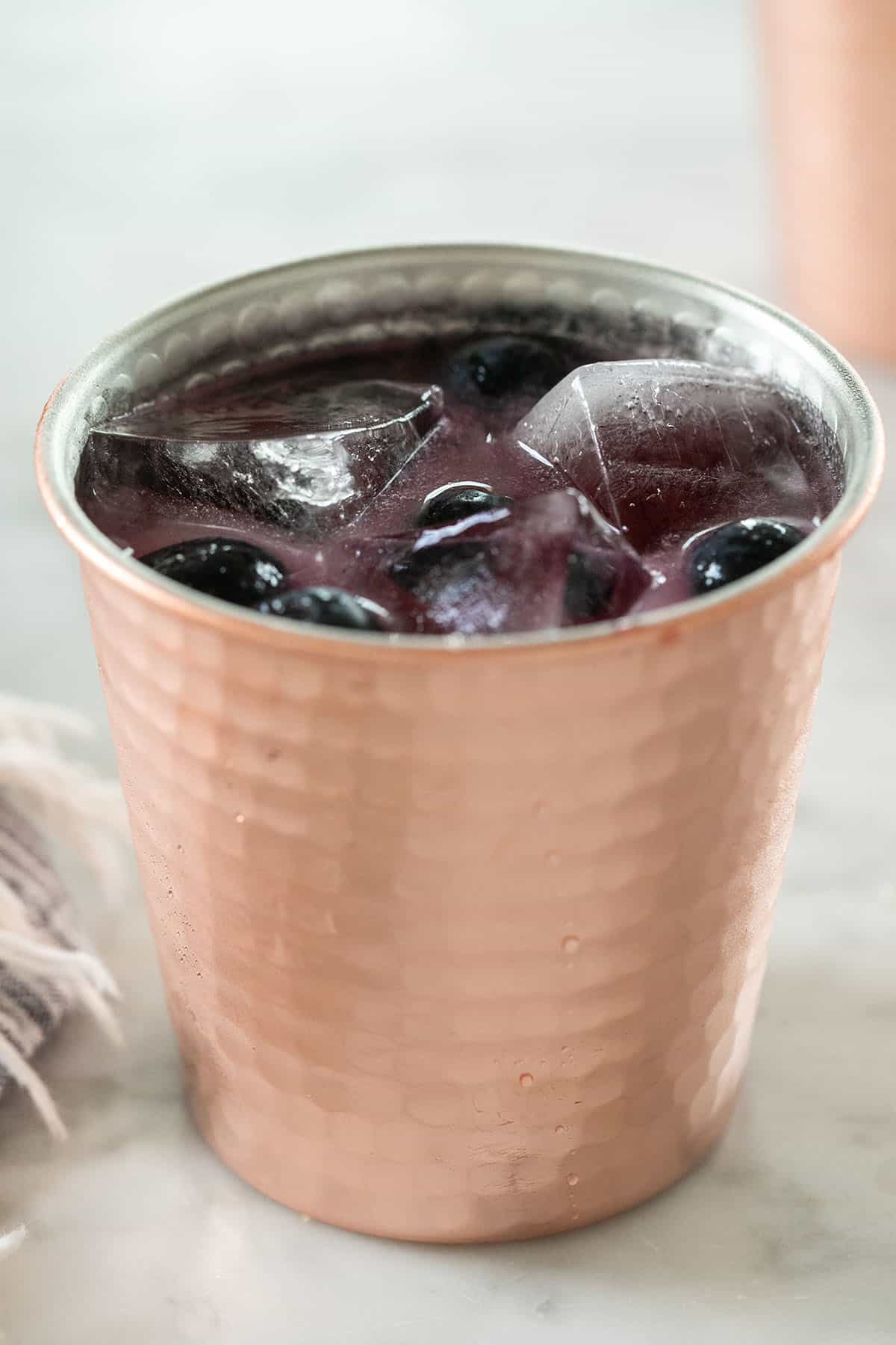 Blueberry cocktail in a copper mug with ice and fresh blueberries.