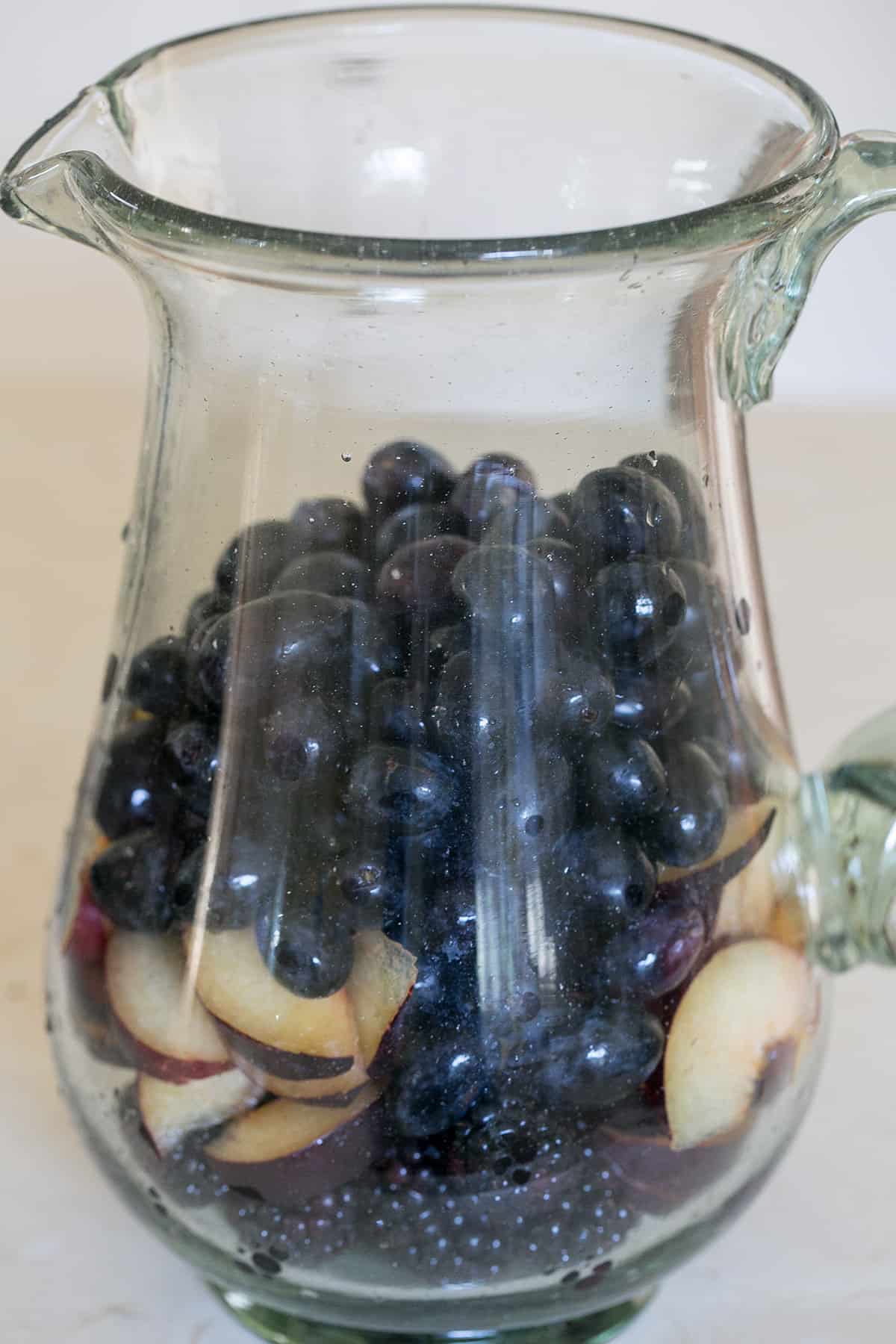 Black grapes, black plums and black fruit in a pitcher.