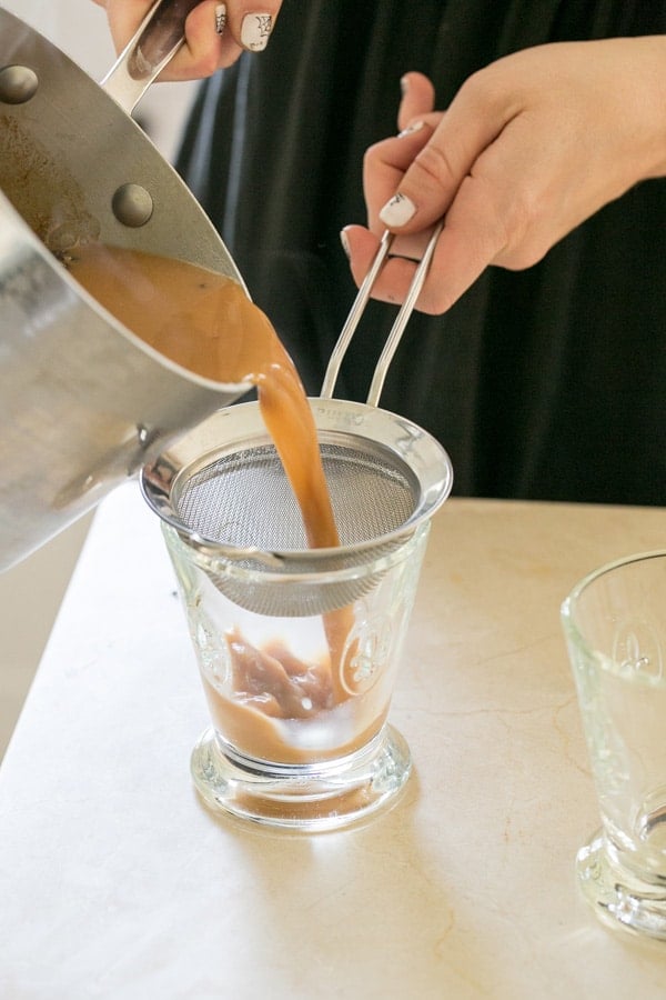 shot of pouring homemade chai tea through a sieve 