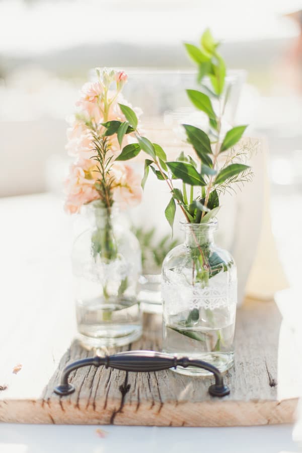 Simple wedding flower arrangements in glass vases on a wooden board.