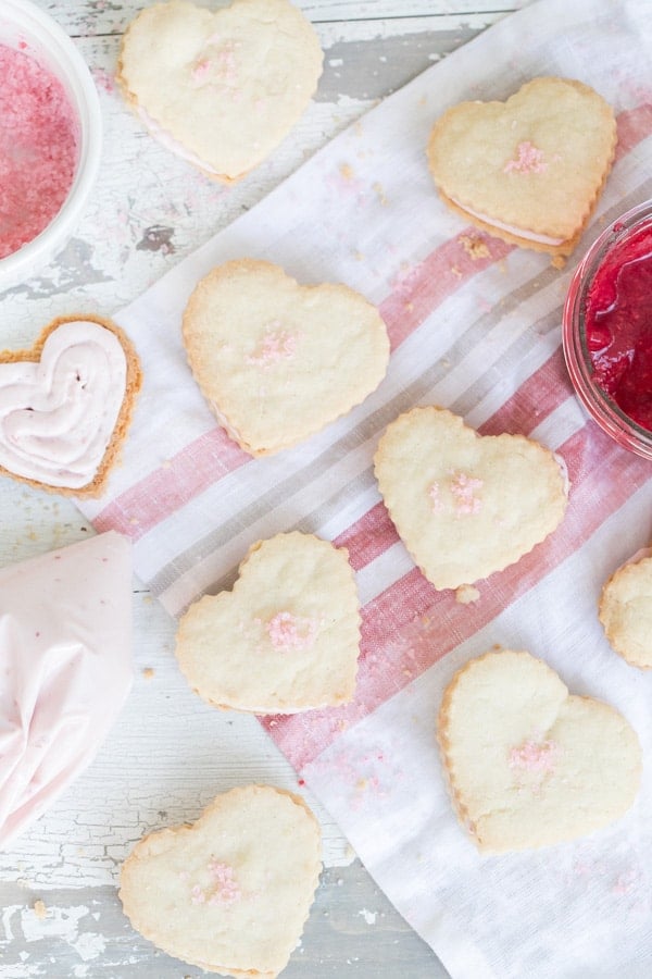 Heart shaped raspberry shortbread cookies with a raspberry white chocolate filling on a pink towel.