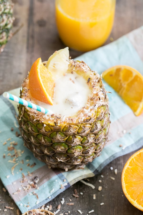 Cocktail in a pineapple cup with a blue straw and oranges 