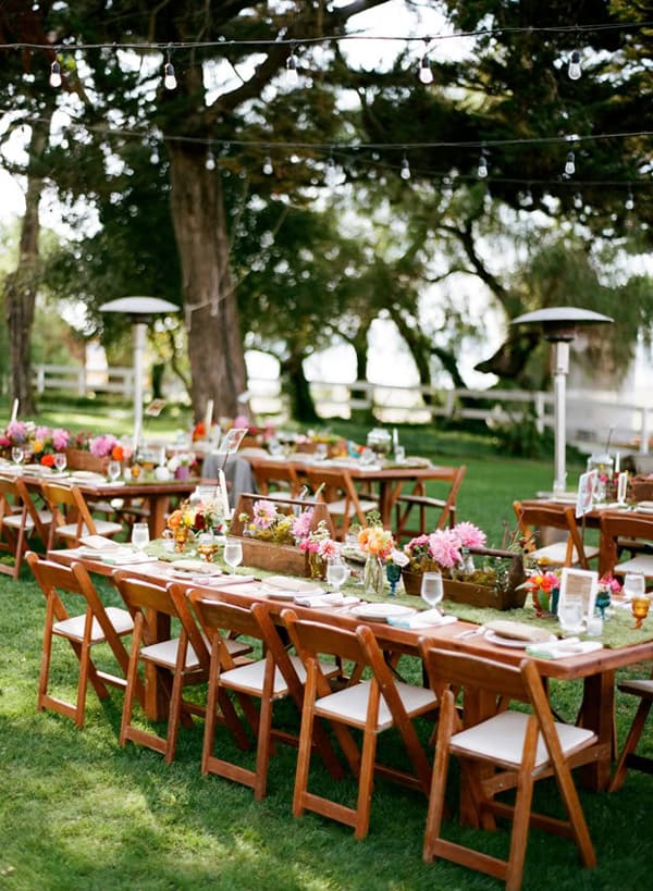 Wooden tables on a green lawn with flowers and a table setting.