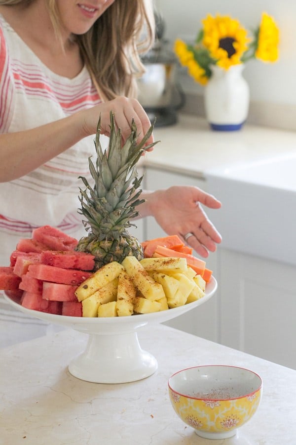 Girl sprinkling chili lime salt on pineapple, watermelon and mango. 