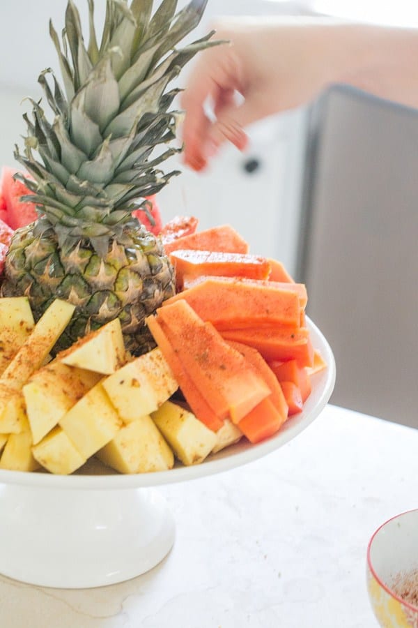 Sprinkling chili lime salt on sliced fruit.