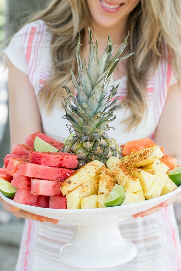 Girl holding platter of pineapple, watermelon and mango with chili lime salt sprinkled on the fruit.