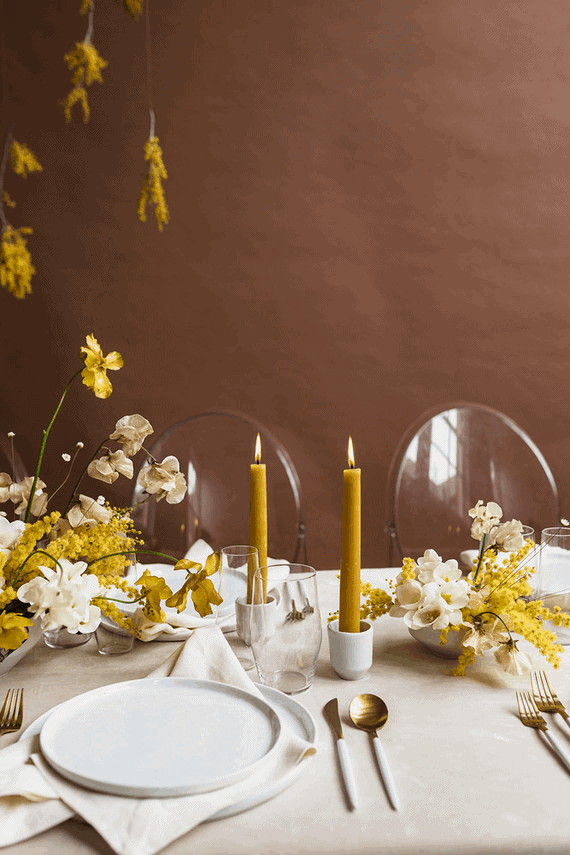 Yellow, white and gold table setting with white plates and gold flatware in a  dining room table