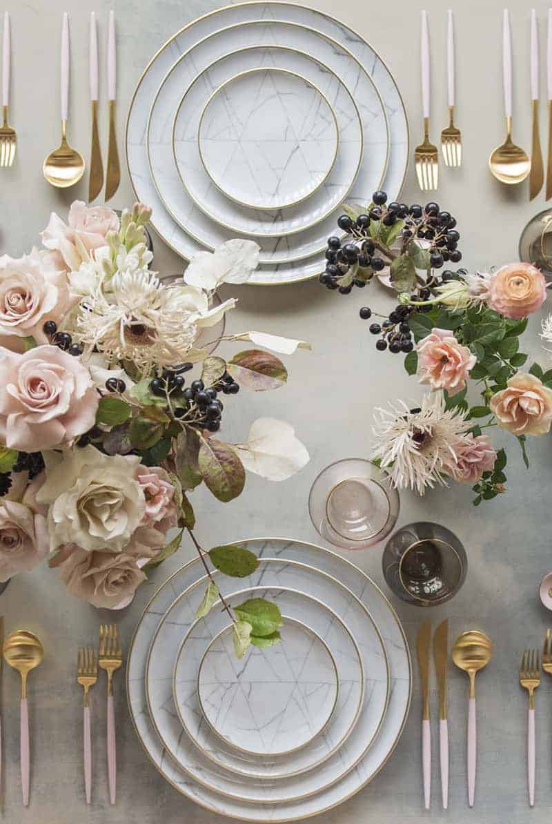 Marble plates with pink flowers and gold and pink flatware with wine glass and pink flowers on a great dining table. 