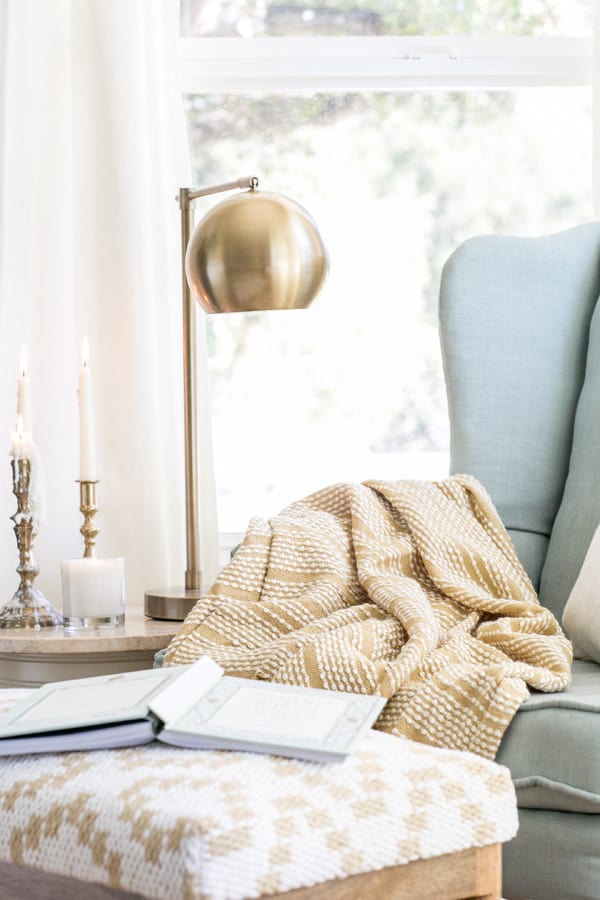 a charming and cozy reading nook with a gold lamp, blue chair and yellow blanket. 