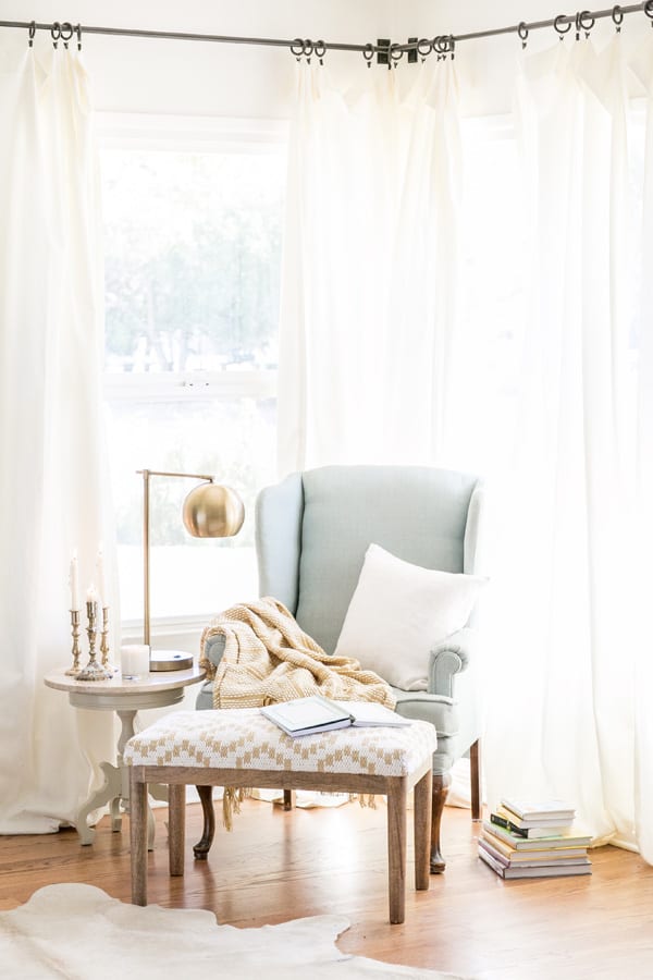 a cozy reading nook with a chair, bench, lamp, pillow and blanket 