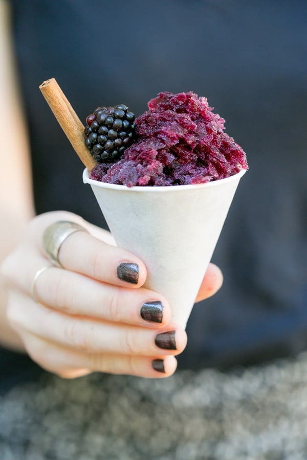 Purple snow cone cup filled with homemade granita. A purple sangria with a cinnamon stick and fresh blackberry.