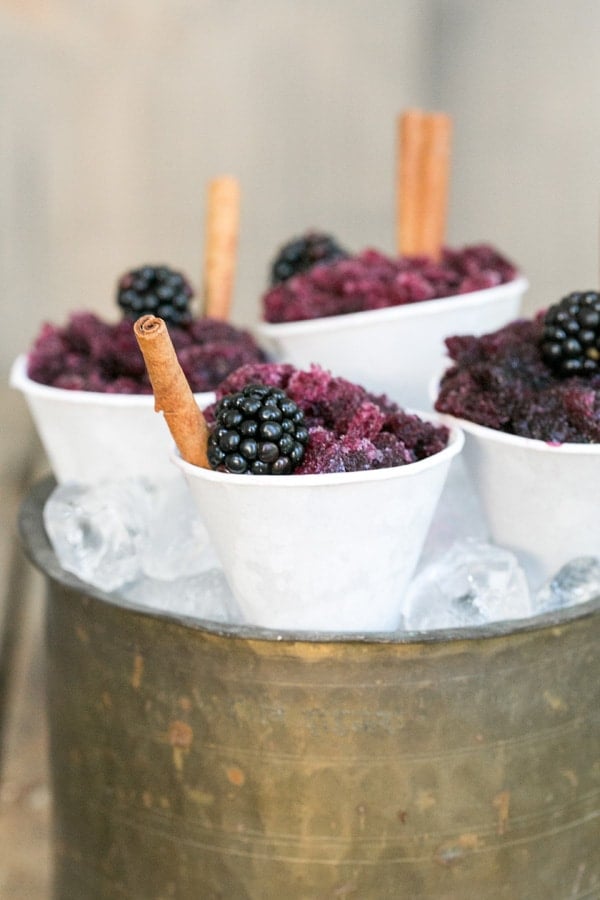 Sangria granita in mini snow cone cups with cinnamon sticks and a blackberry.