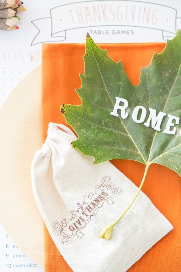 Kids Thanksgiving table with orange napkins, bamboo plates, leaf with names and a give thanks drawstring bag. 