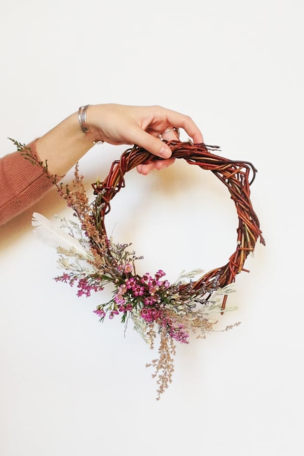 Girl holding a DIY willow wreath with dried flowers on a white wall - tracking information