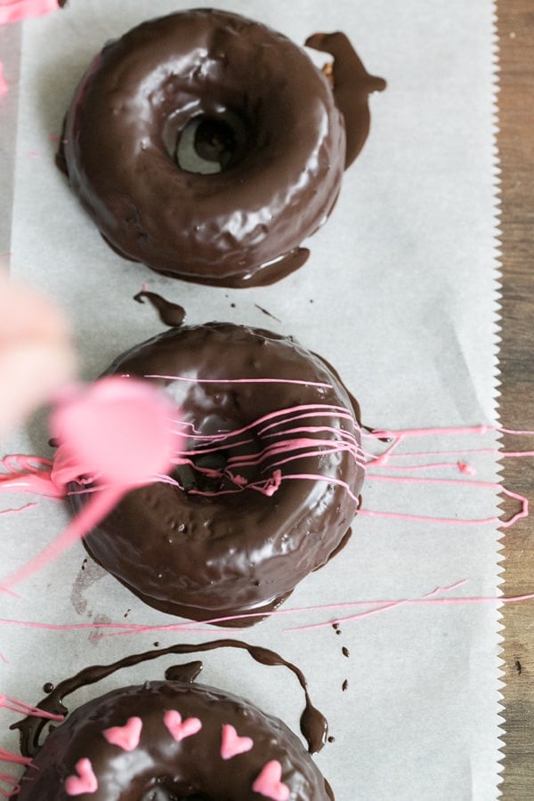 overhead shot of pink chocolate being drizzled onto chocolate donuts