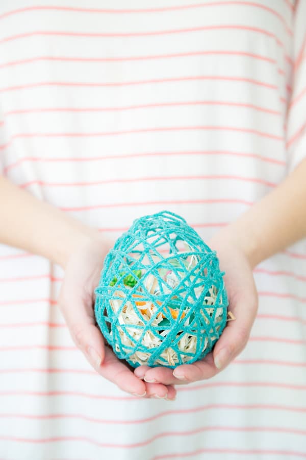 Girl holding an Easter egg made from yarn with treats inside.