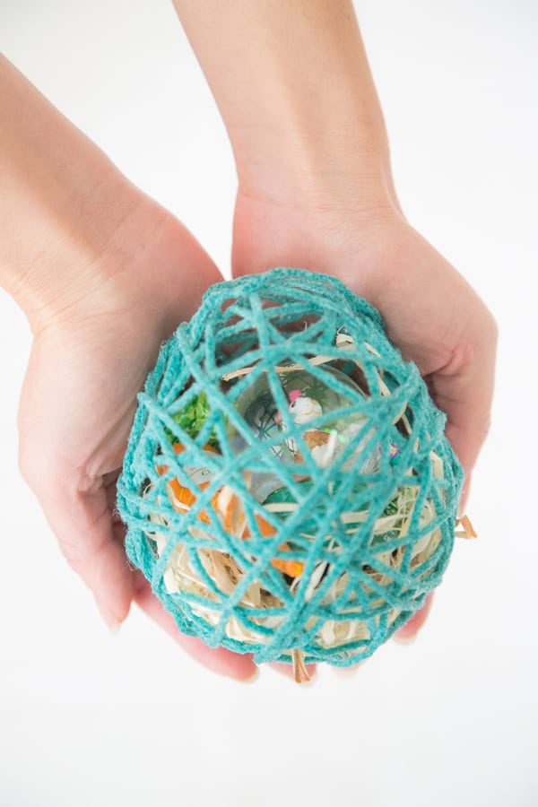 Girl holding an Easter egg made from yarn with treats inside.