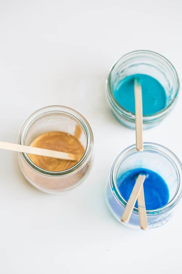 blue, gold and turquoise paint in jars with wooden stir sticks.