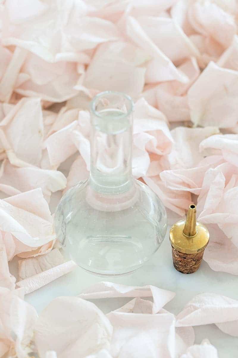 Small bottle of rose water on a table with rose petals. - fresh roses