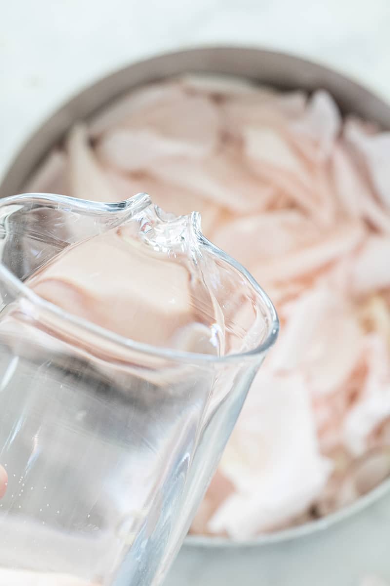 Pouring distilled water into a pot of rose petals - benefits of rose water