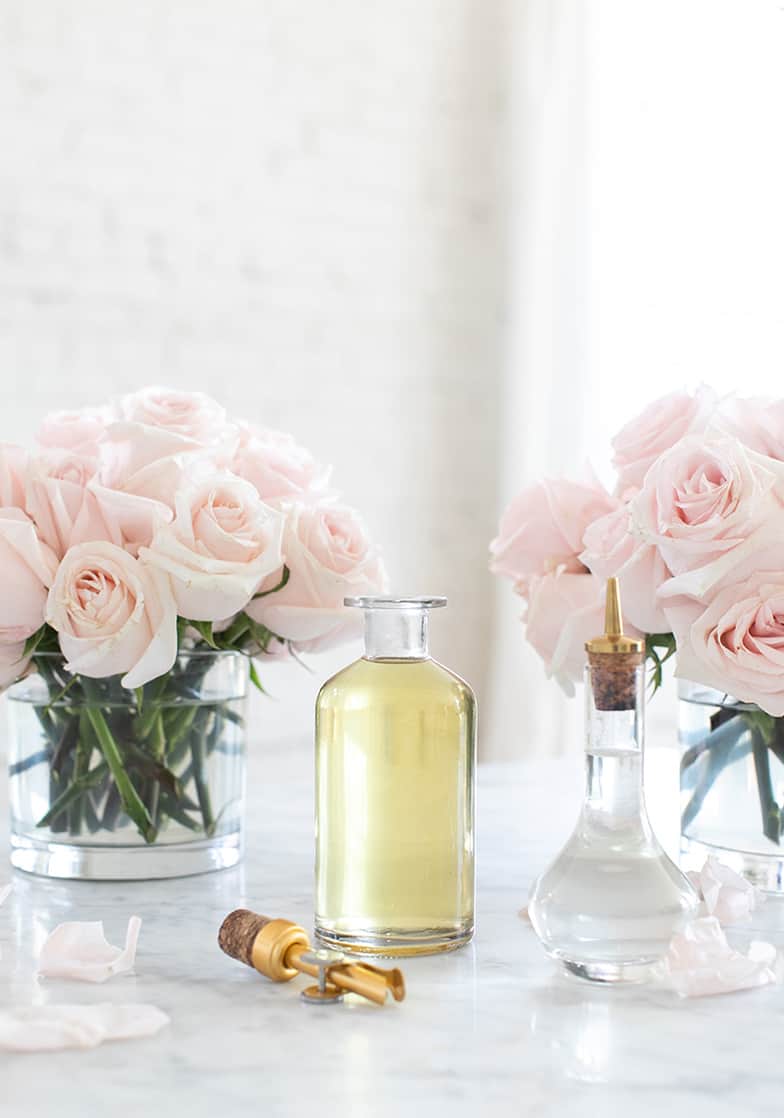 Two bottles of rose water with pink roses in the back - homemade rose water