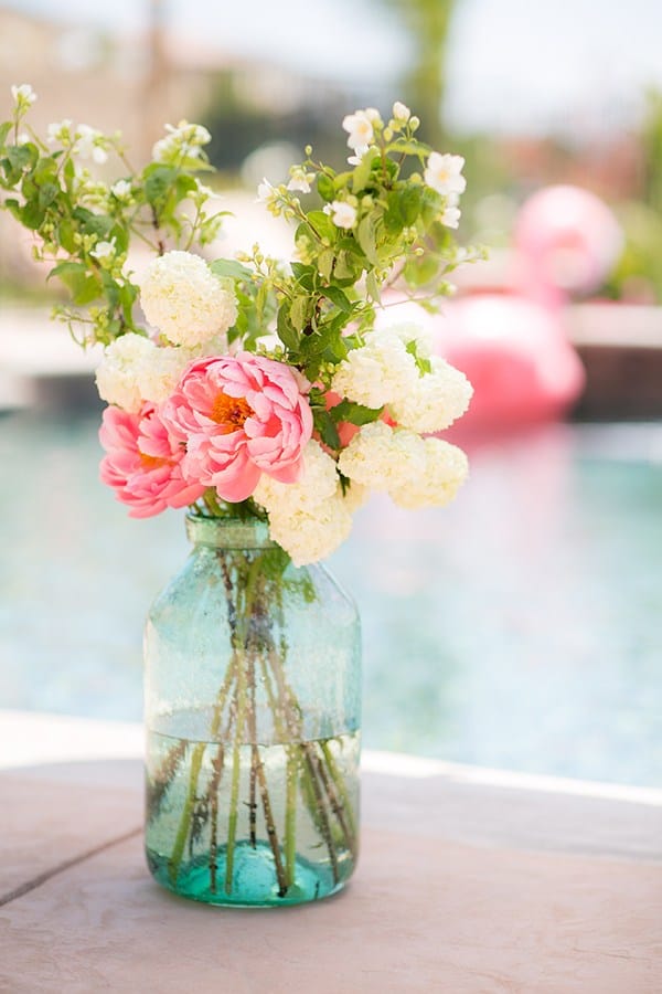 Flower arrangement in a large green glass vase next to a flamingo pool party