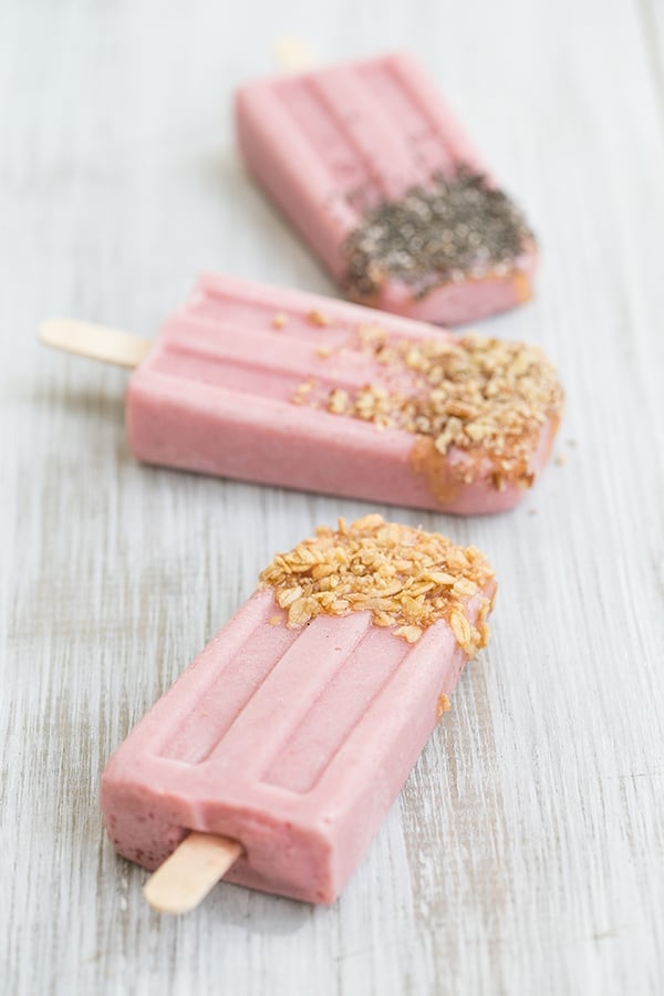 Three dairy free strawberry banana popsicles with toppings.