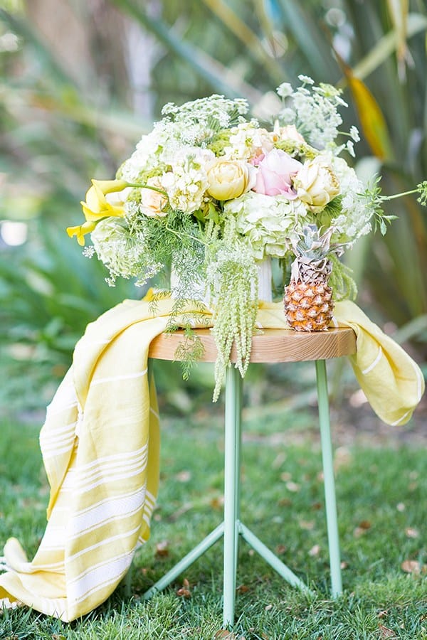 Yellow flowers on a stool with a yellow towel and baby pineapple.