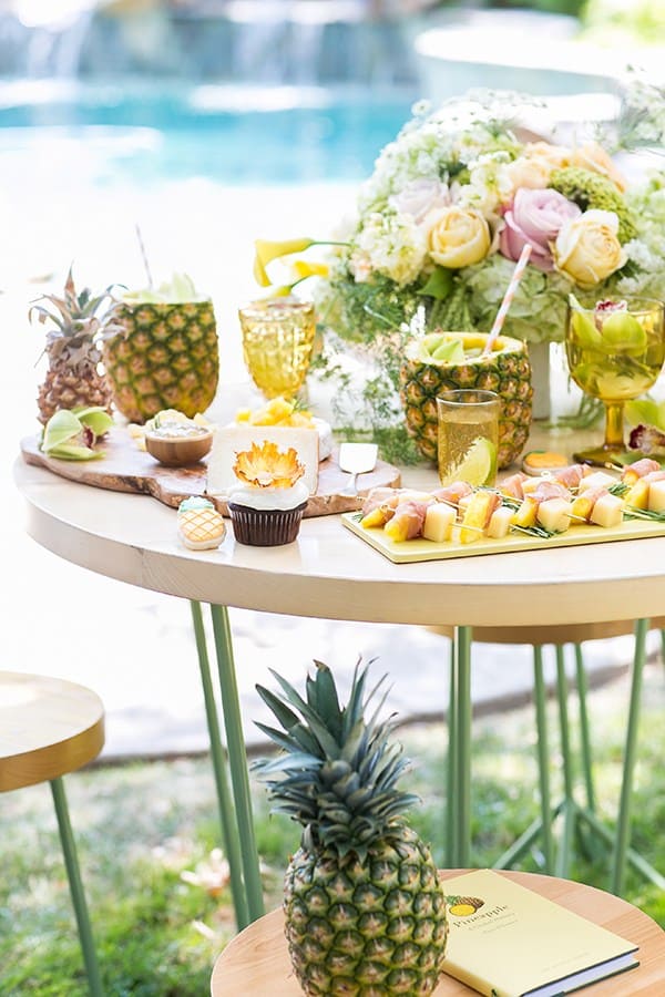 Table with pineapples, flowers, desserts for a pineapple party.