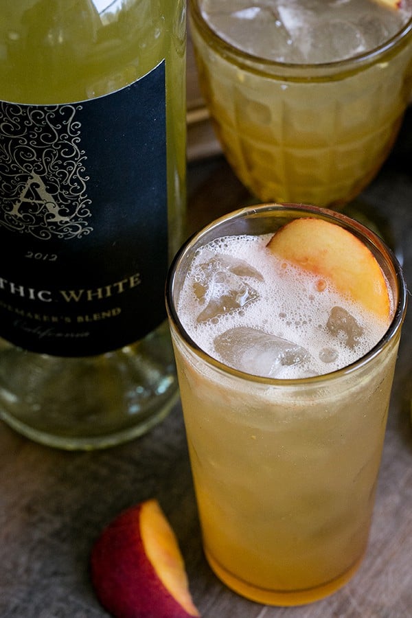 A white wine cocktail served in a tall yellow glass, garnished with a slice of peach.