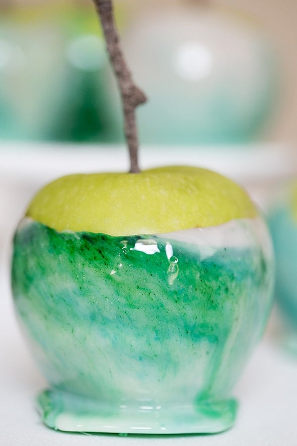 A green, candy marbled apple with  a stick in it.
