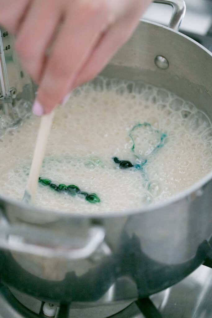 Adding gel food coloring to melted sugar for marbled candy apples.