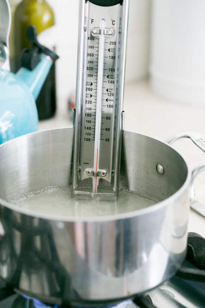 A candy thermometer clipped to a pot of candy apple syrup.