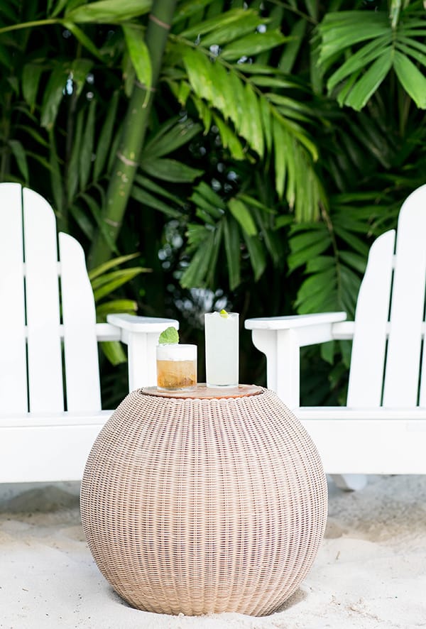 Two chairs and on a beach with a table and cocktails. 