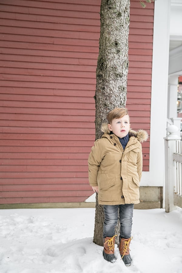 Little boy standing by a tree in snow.