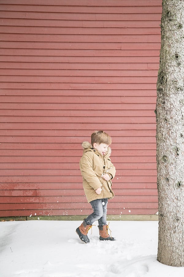 Little boy in snow by red house